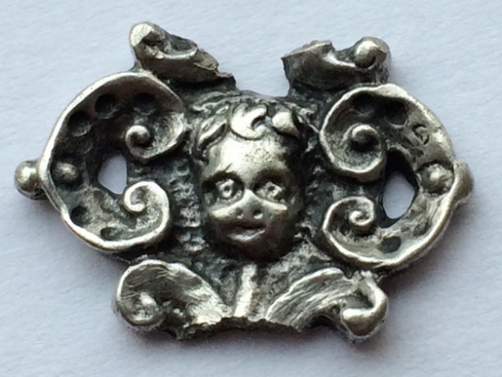 Stukje van een zilveren kledinghaakje met een cherubijnenkopje